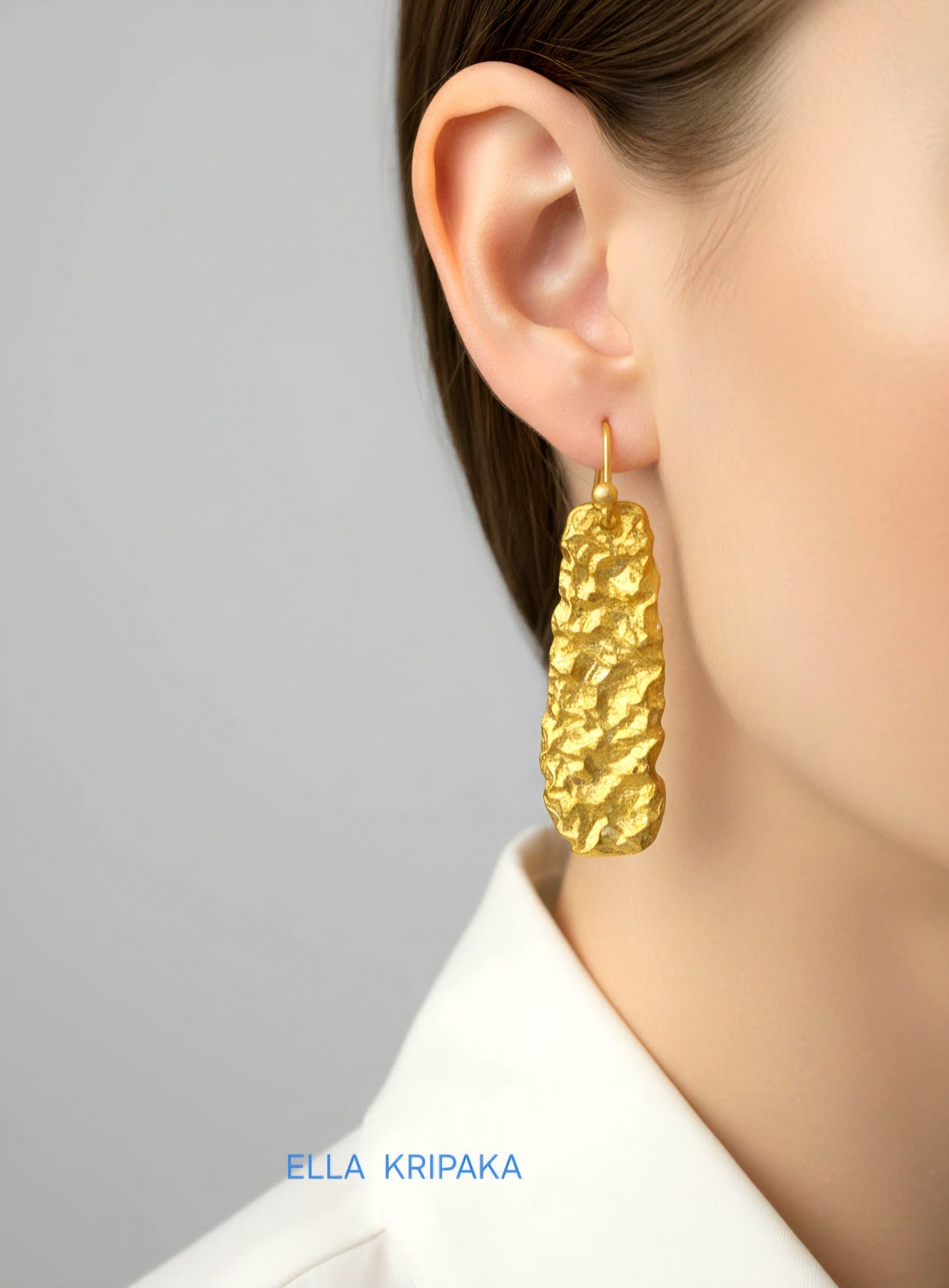Organic 24k 9999 gold hammered wavy earrings with shiny gold textures worn by a woman and on grey background, artist-jeweler's name 'Ella Kripaka'