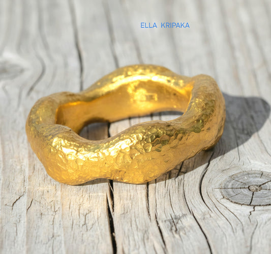 Hammered 24k 9999 Gold thick uneven wavy ring organic with textured gold on a light old wooden background, branded 'Ella Kripaka'