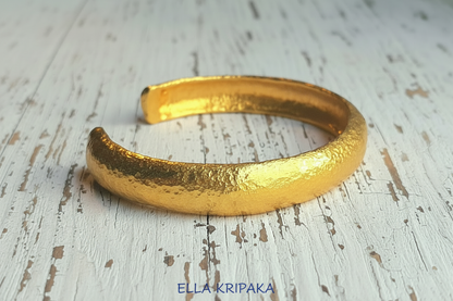 24k 9999 gold hammered Ancient Rome style bracelet cuff on old wooden background, indicating it is a custom-made jewelry with creator's name 'Ella Kripaka'