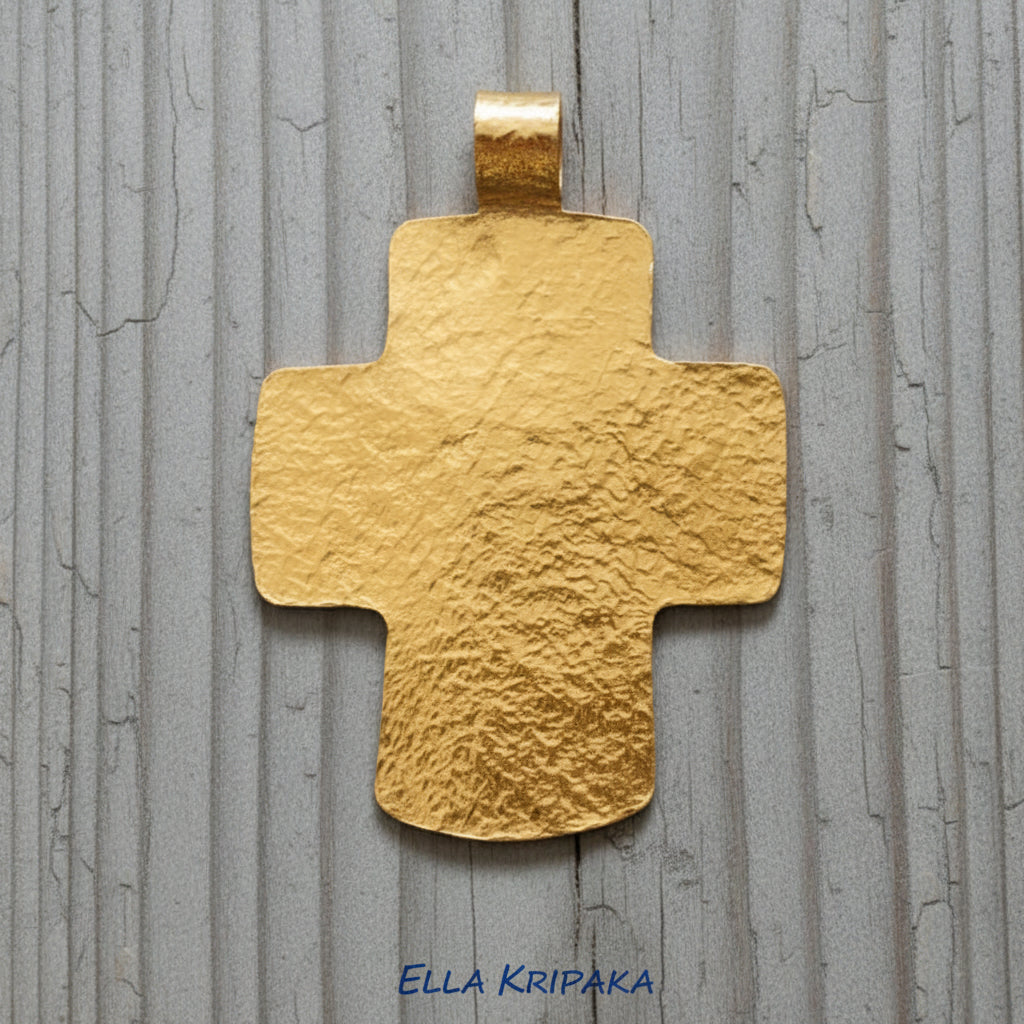 Hammered 24k gold textured cross pendant on a grey rustic wooden surface, artist-jeweler 'Ella Kripaka' branding