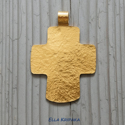 Hammered 24k gold textured cross pendant on a grey rustic wooden surface, artist-jeweler 'Ella Kripaka' branding
