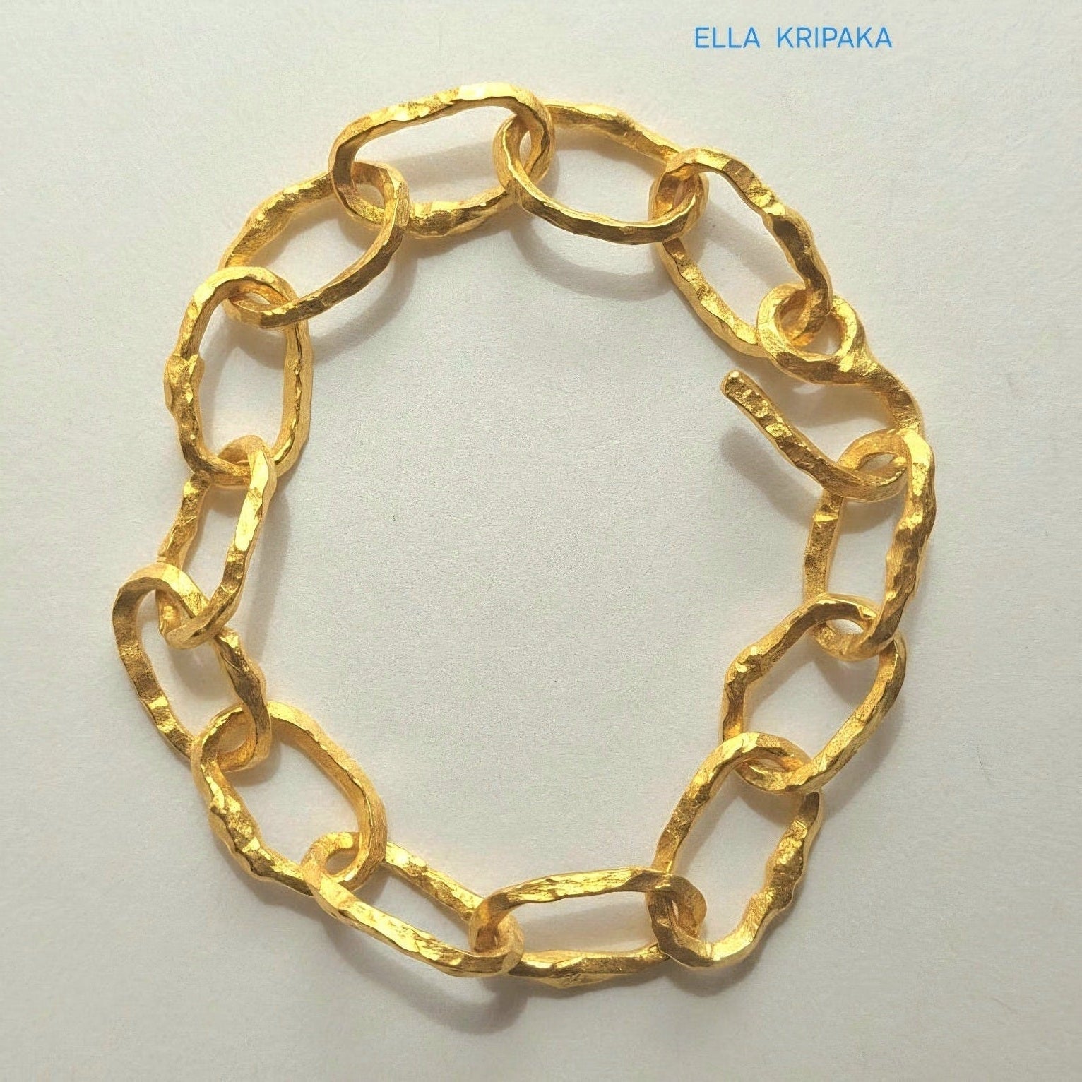 Hammered 24k gold organic bracelet chain with  uneven textures and a thick hook clasp on light beige paper surface, branding artist name 'Ella Kripaka'