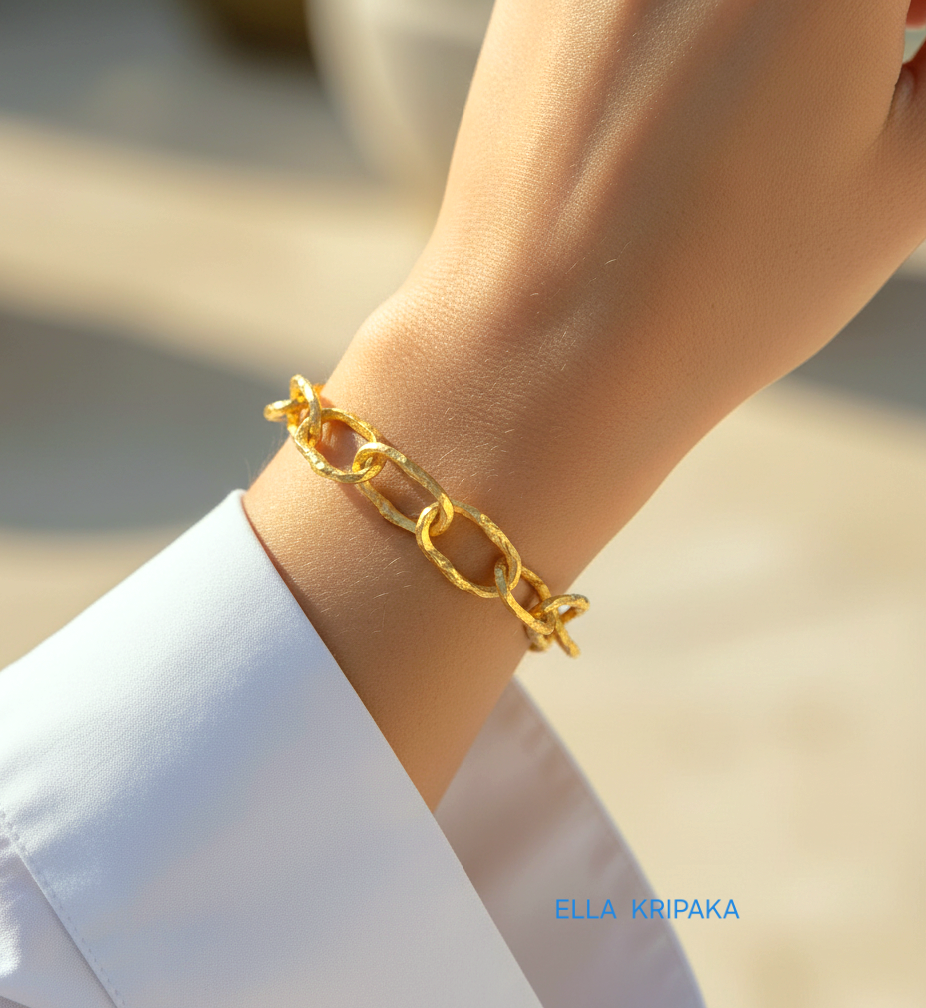 Hammered 24k gold organic bracelet chain with uneven textures is worn by a woman on wrist and on blurred background, branding artist name 'Ella Kripaka'