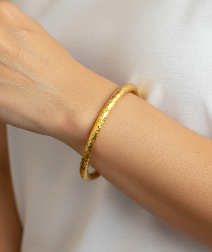Hammered 24k 9999 gold bangle thick bracelet Ancient Rome style worn on wrist by a model and on a white background, branding artist-jeweler name 'Ella Kripaka'