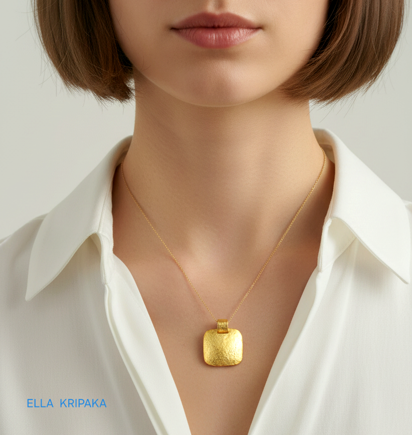 Hammered 24k gold textured convex square pendant with thin chain worn by a woman with white shirt, and with 'Ella Kripaka' branding