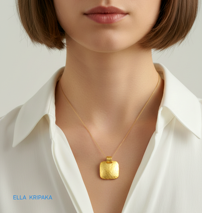 Hammered 24k gold textured convex square pendant with thin chain worn by a woman with white shirt, and with 'Ella Kripaka' branding
