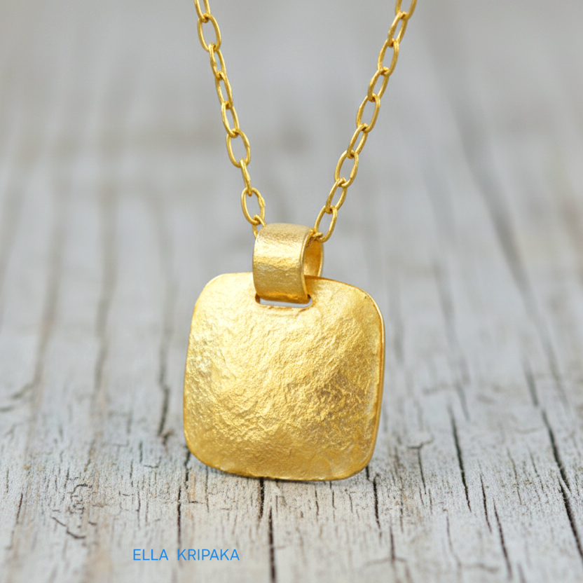 Hammered 24k gold textured convex square pendant with chain on light grey rustic wooden surface with 'Ella Kripaka' branding