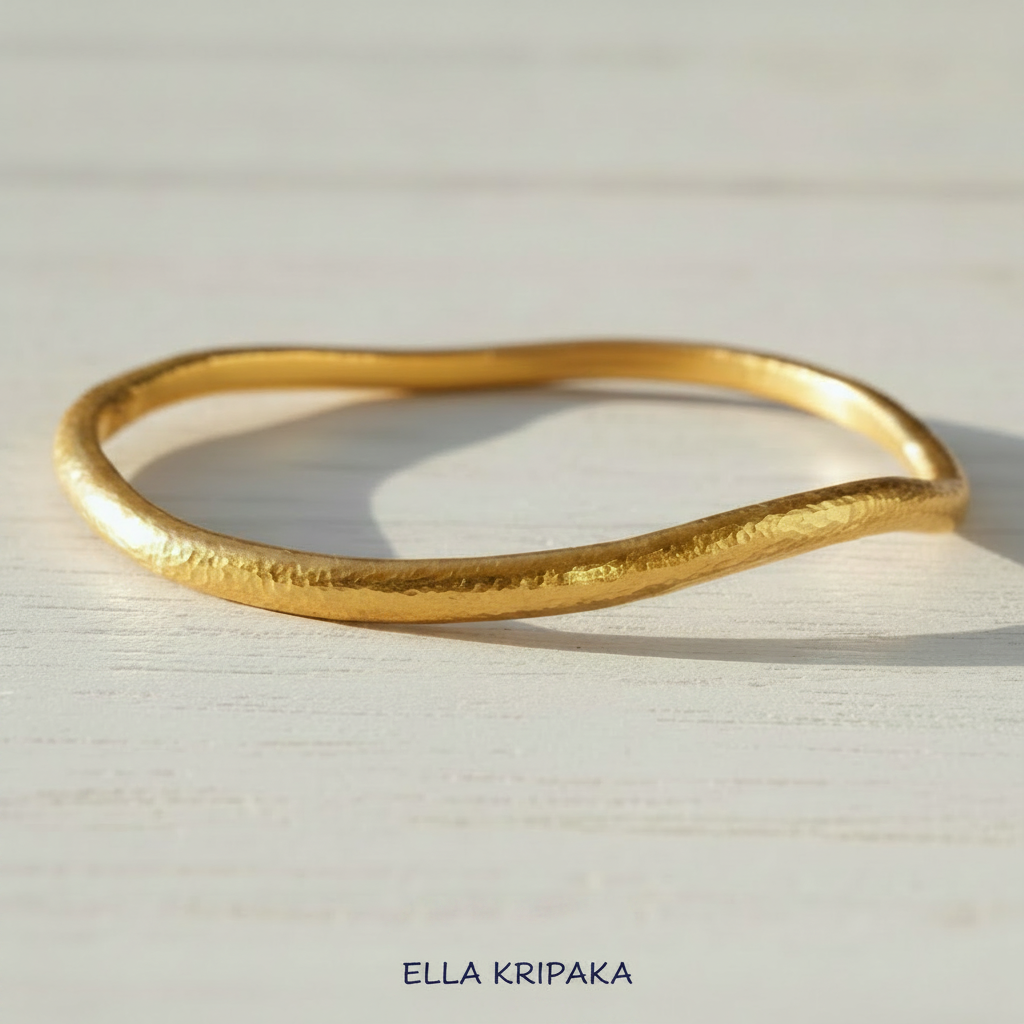 Organic 24k gold hammered bangle thick bracelet with uneven shape on light wooden surface, artist-jeweler 'Ella Kripaka'
