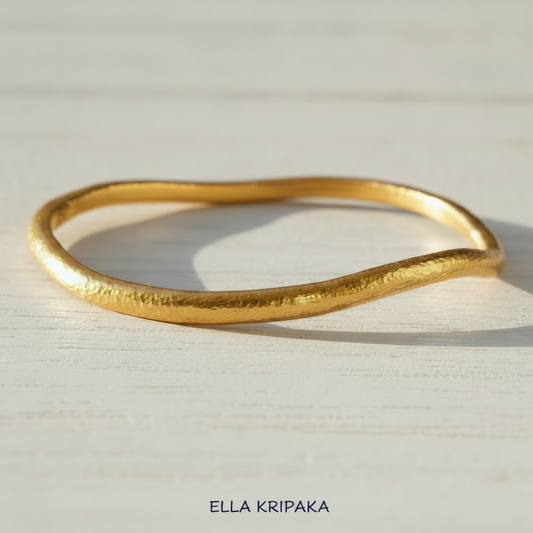 Organic 24k gold hammered bangle thick bracelet with uneven shape on light wooden surface, artist-jeweler 'Ella Kripaka'