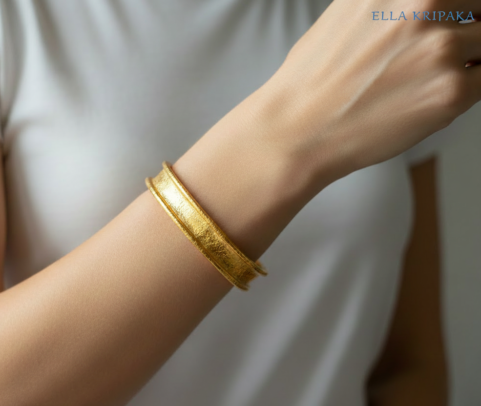 Hammered 24k 9999 Gold thick bangle bracelet Ancient Rome style worn by woman on wrist and on white t-shirt background, artist's name 'Ella Kripaka' branding
