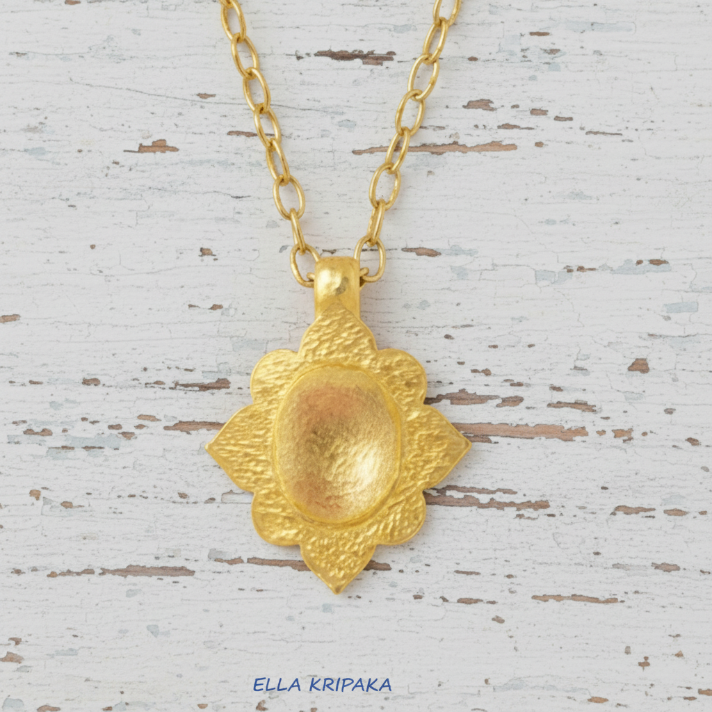 24k gold hammered textured dome pendant with Byzantune ornament and with gold chain is on white rustic wooden surface, with artist-jeweler 'Ella Kripaka' branding