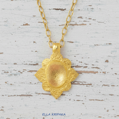 24k gold hammered textured dome pendant with Byzantune ornament and with gold chain is on white rustic wooden surface, with artist-jeweler 'Ella Kripaka' branding