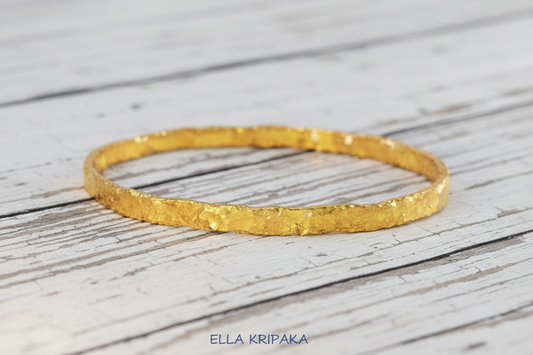Organic hammered 24k 9999 Gold thick bangle uneven bracelet on a wooden background, artist's name 'Ella Kripaka' branding