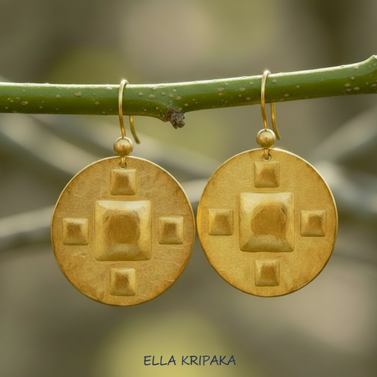 Hammered 24k 9999 Hammered 24k Gold disk earrings with five convex squares are hanging on a branch with 'Ella Kripaka' branding