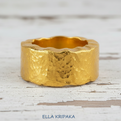 Organic hammered 24k 9999 Gold wavy ring band with thick wavy edges and with forged gold textures on white old wooden surface, artist-jeweler's name 'Ella Kripaka' branding