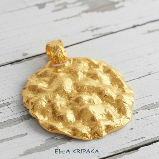 Organic 24k 9999 gold hammered uneven disk pendant on a white wooden surface, branded 'Ella Kripaka'