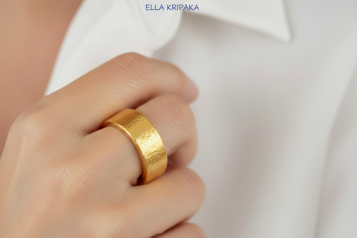 Hammered 24k 9999 Gold thick ring Ancient Rome style with a textured gold on person's finger on blurred white shirt backgroud, branded 'Ella Kripaka' artist-jeweler