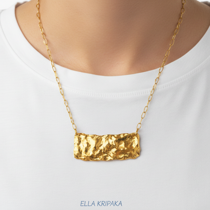 Hammered 24k Gold organic uneven wavy rectangular pendant with chain wearing on person in a white t-shirt, artist's name 'Ella Kripaka' 