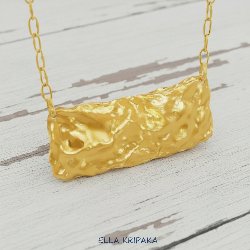 Hammered 24k 9999 Gold organic uneven wavy pendant with chain on a white old wooden surface, artist's name 'Ella Kripaka' 