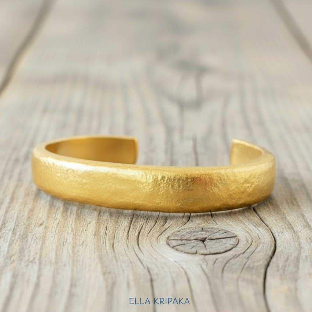 Hammered 24k 9999 Gold thick cuff bracelet Ancient Rome style on a wooden background with 'Ella Kripaka' branding