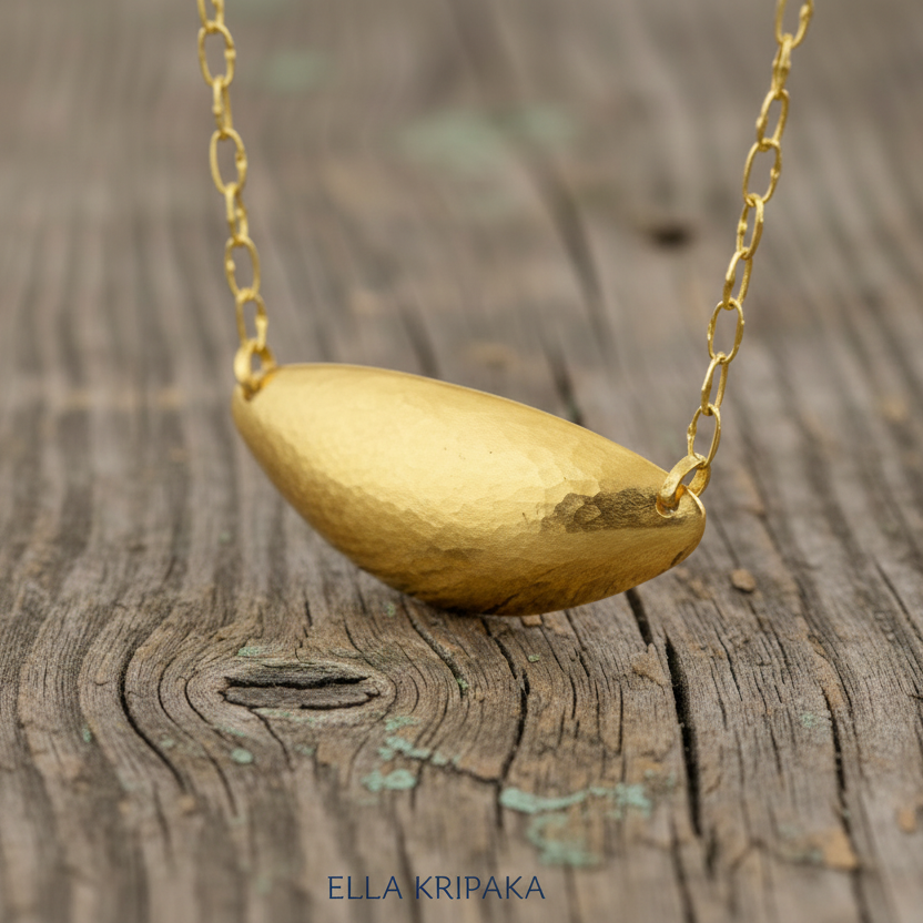 24k 9999 gold hammered dome pendant with forged gold textures and with chain is on a old wooden surface, artist's name 'Ella Kripaka'