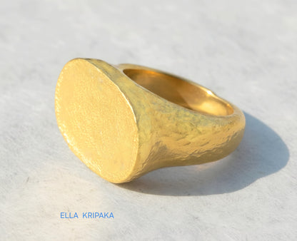 Hammered 24k 9999 Gold ring thick signet Ancient Egypt style and Ancient Rome style and with forged textured gold on a white paper surface, artist-jeweler's name 'Ella Kripaka' branding