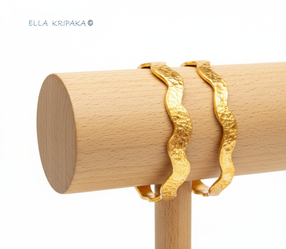 Wavy 24k gold 9999 gold hammered two bangles thick bracelets Ancient Rome style on wooden stand against white background, artist-jeweler 'Ella Kripaka'