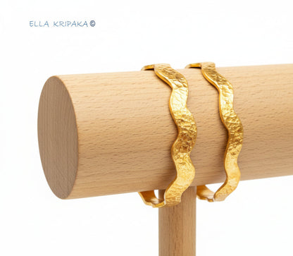 Wavy 24k gold 9999 gold hammered two bangles thick bracelets Ancient Rome style on wooden stand against white background, artist-jeweler 'Ella Kripaka'