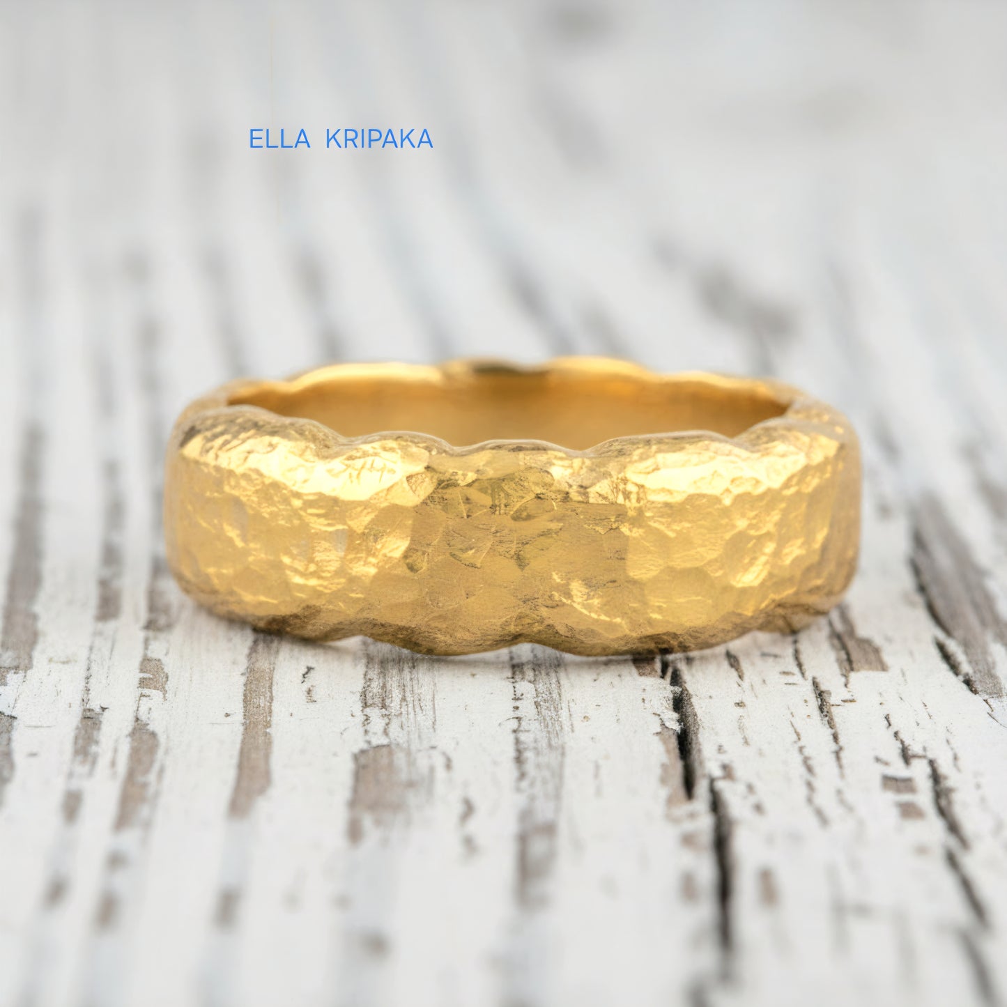 Organic hammered 24k 9999 gold wavy ring band and with forged gold textures on white old wooden surface, artist-jeweler's name 'Ella Kripaka' branding