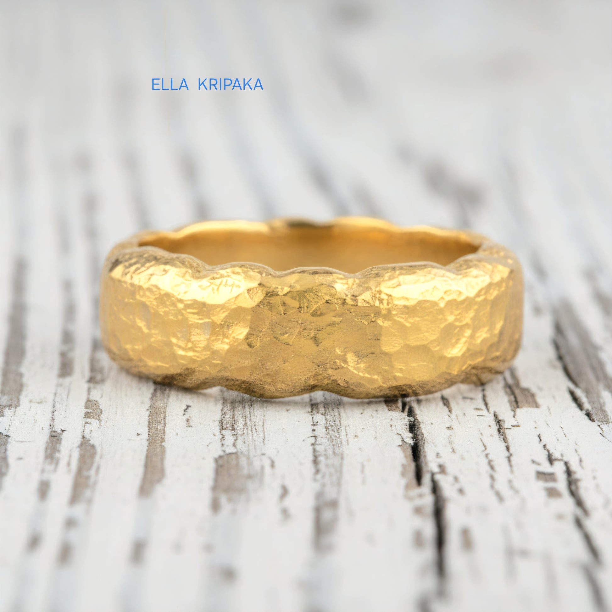 Organic hammered 24k 9999 gold wavy ring band and with forged gold textures on white old wooden surface, artist-jeweler's name 'Ella Kripaka' branding