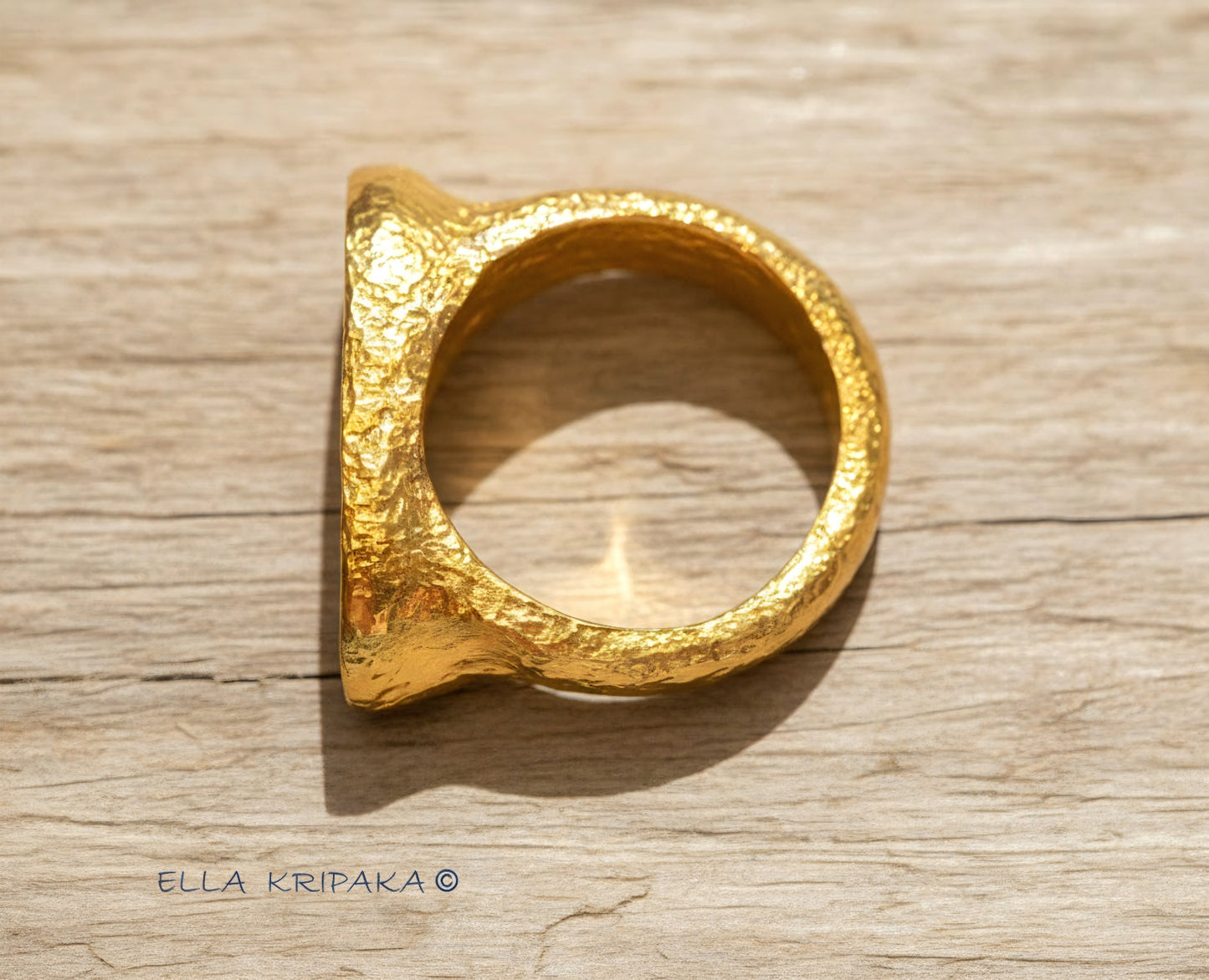Hammered 24k 9999 Gold ring thick signet Ancient Egypt style and Ancient Rome style and with forged textured gold on a light old wooden surface, artist-jeweler's name 'Ella Kripaka' branding