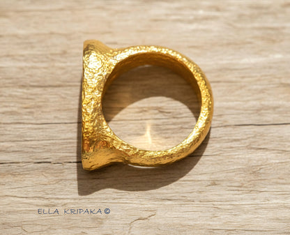 Hammered 24k 9999 Gold ring thick signet Ancient Egypt style and Ancient Rome style and with forged textured gold on a light old wooden surface, artist-jeweler's name 'Ella Kripaka' branding