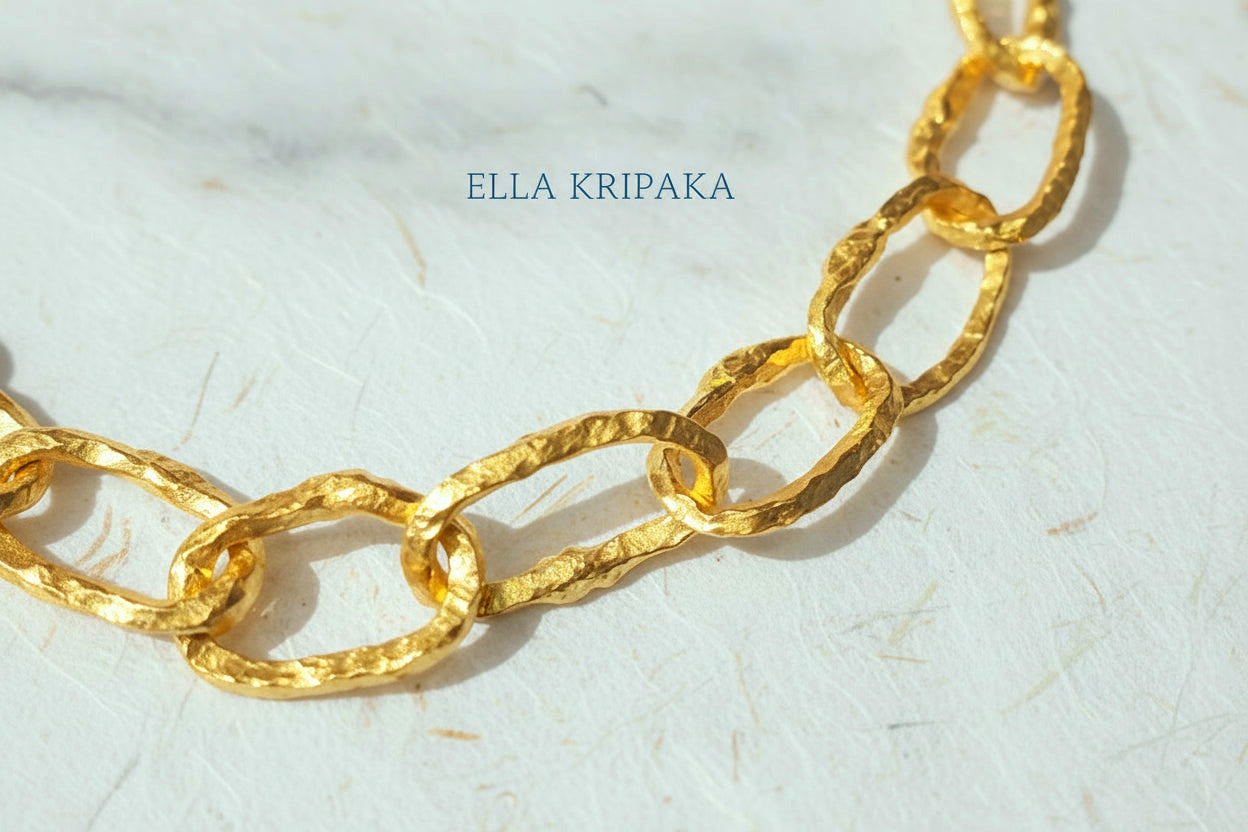 Hammered 24k gold organic bracelet chain with  uneven textures and a thick hook clasp on white craft paper surface, branding artist name 'Ella Kripaka'