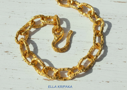 Hammered 24k 9999 gold organic necklace chain with hammered uneven textures and a thick hook clasp on white wooden surface, artist name 'Ella Kripaka'