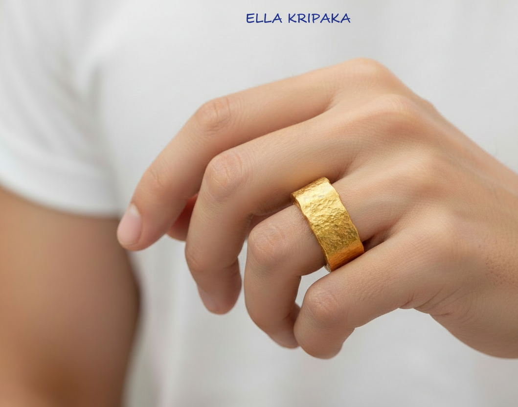 Organic hammered 24k 9999 Gold wavy ring band with thick wavy edges and with forged gold textures is worn by a man on finger and on white surface, artist-jeweler's name 'Ella Kripaka' branding