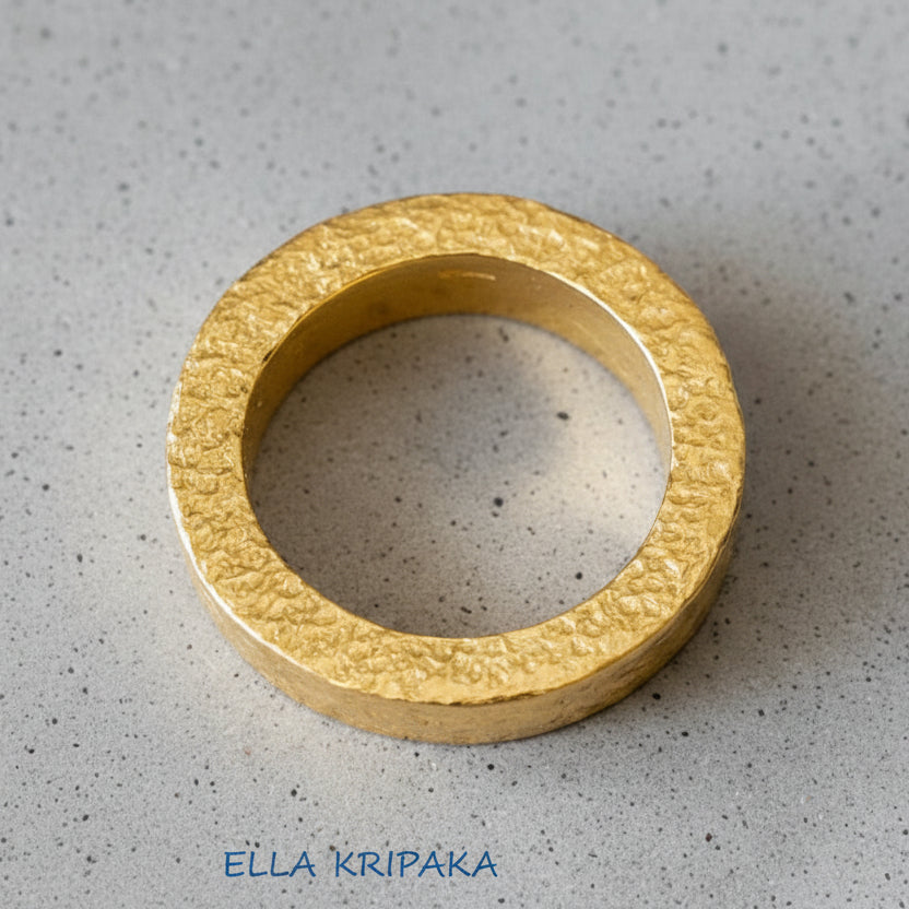 Hammered 24k Gold 9999 gold ring thick and with textured surface on a grey background, branded 'Ella Kripaka'