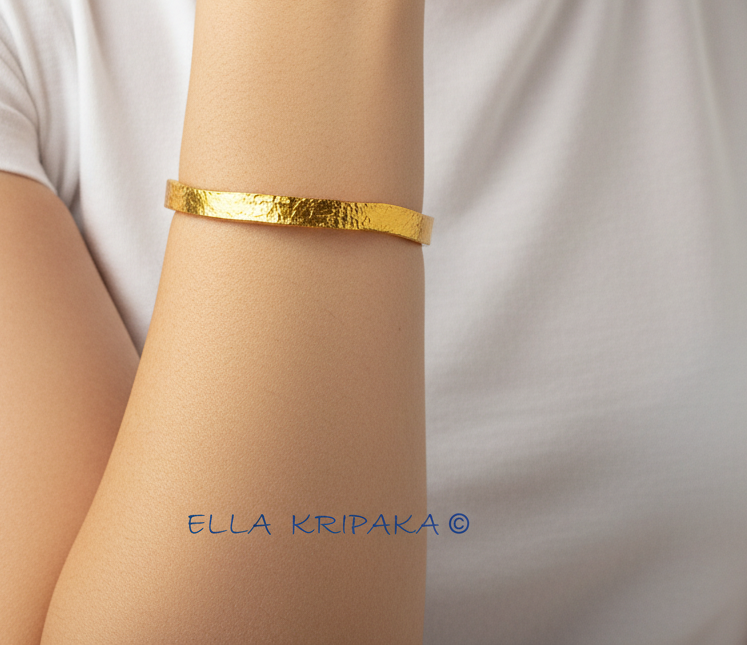 Organic 24k 9999 gold hammered uneven bangle thick bracelet worn by a model on wrist and on white t-shirt background, artist-jeweler 'Ella Kripaka'