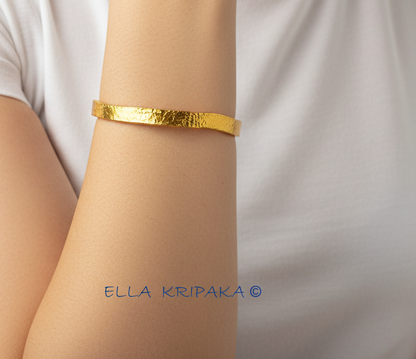 Organic 24k 9999 gold hammered uneven bangle thick bracelet worn by a model on wrist and on white t-shirt background, artist-jeweler 'Ella Kripaka'