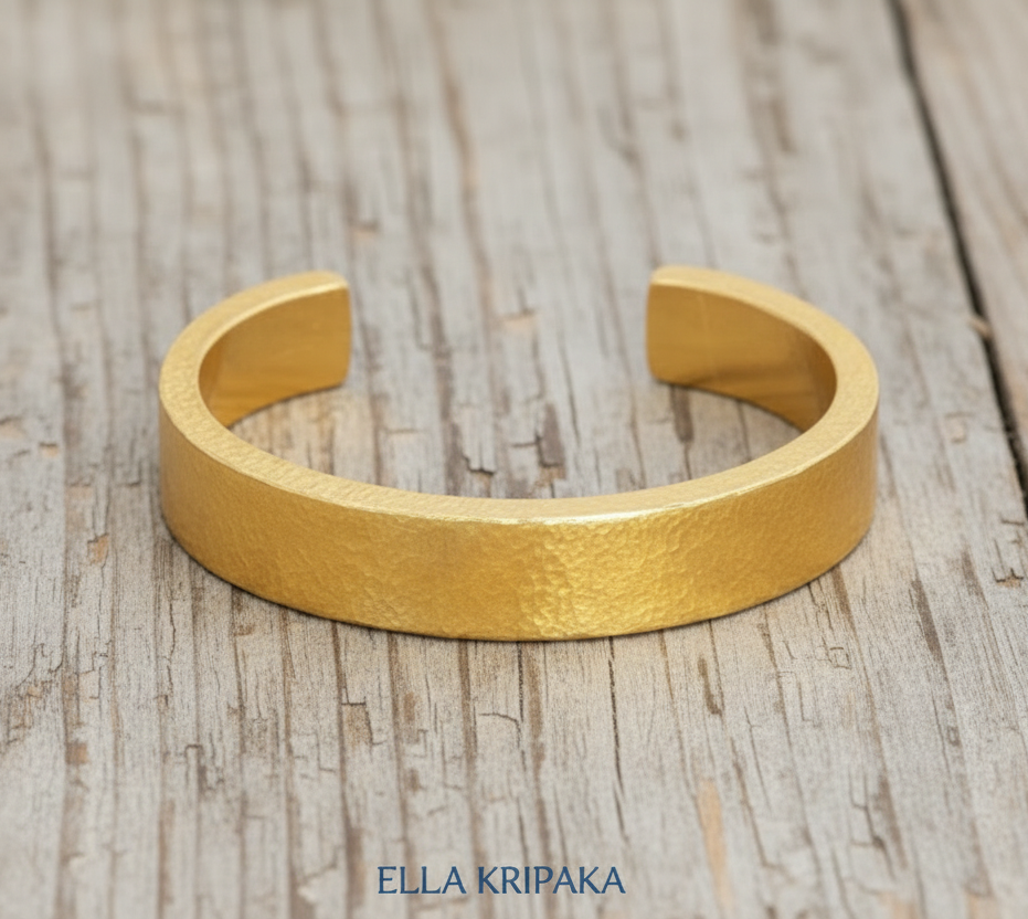 Hammered 24k 9999 Gold thick cuff bracelet Ancient Rome style on a wooden background with 'Ella Kripaka' branding