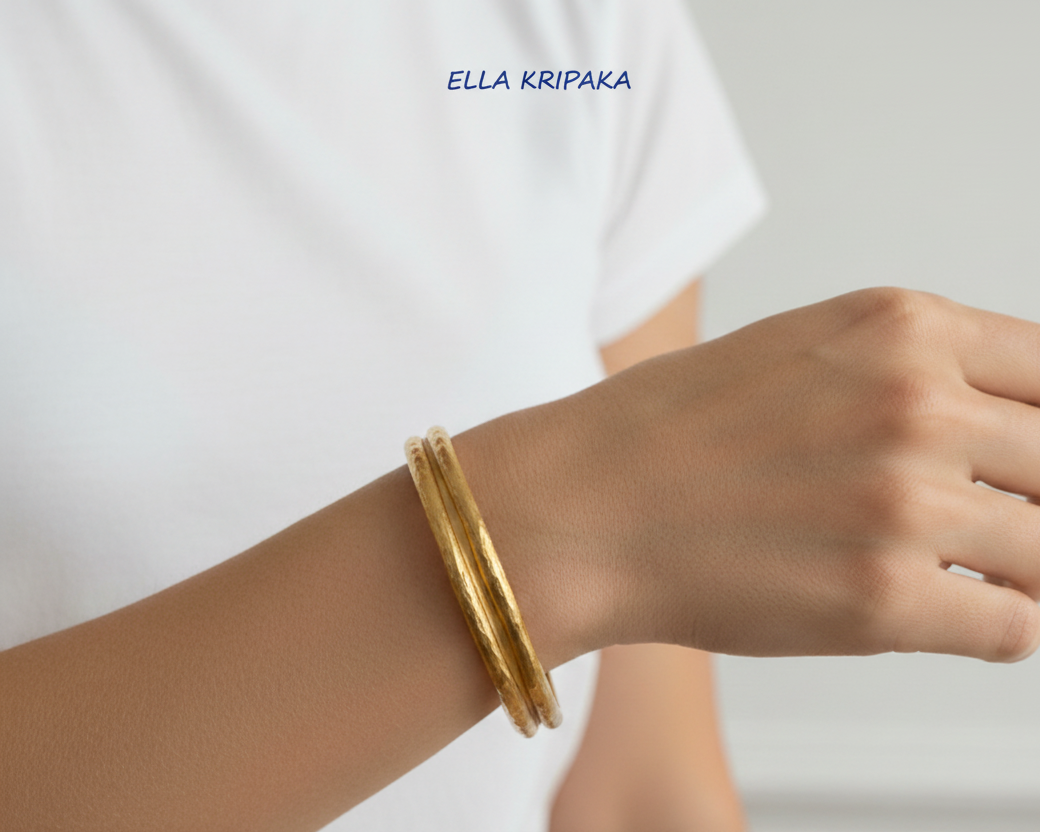 Organic hammered 24k 9999 Gold thick bangle uneven bracelet worn by a person on wrist and with white t-shirt background, artist's name 'Ella Kripaka' branding