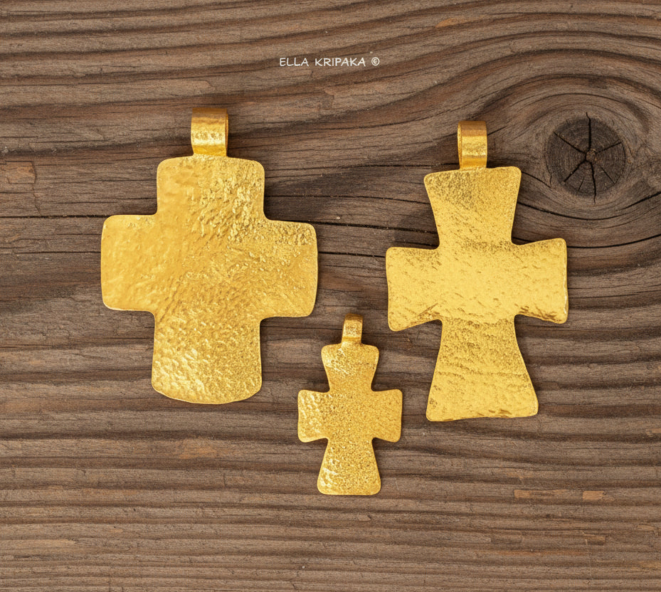 Three hammered 24k gold textured crosses pendants on a rustic wooden surface, artist-jeweler 'Ella Kripaka' branding