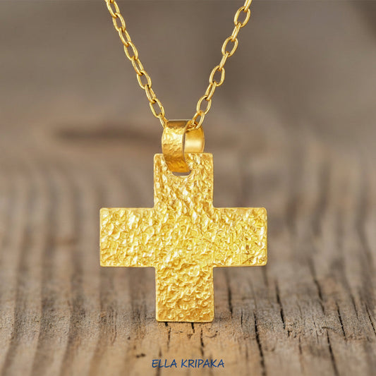 24k Gold hammered Byzantine Cross pendant on thick chain and with a textured design on rustic wooden surface, branded artist-jeweler 'Ella Kripaka'
