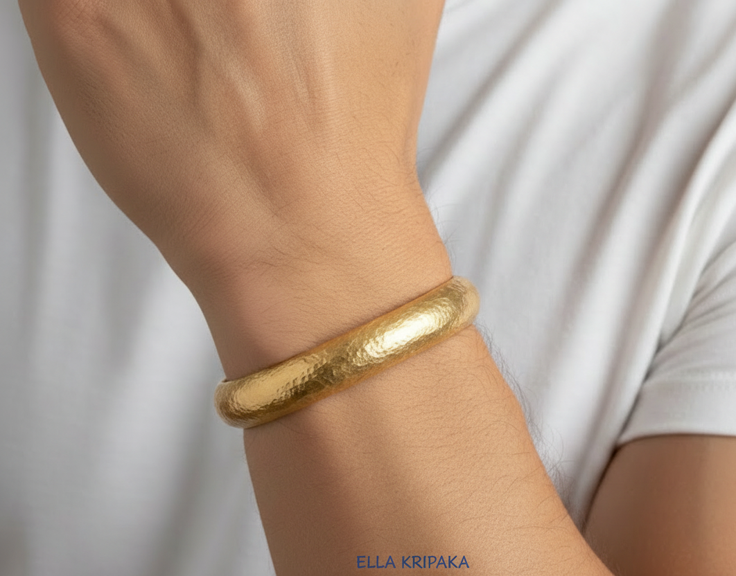 24k 9999 gold hammered Ancient Rome convex bracelet cuff worn on man's wrist with a white t-shirt background, indicating it is a custom-made jewelry with creator's name 'Ella Kripaka'