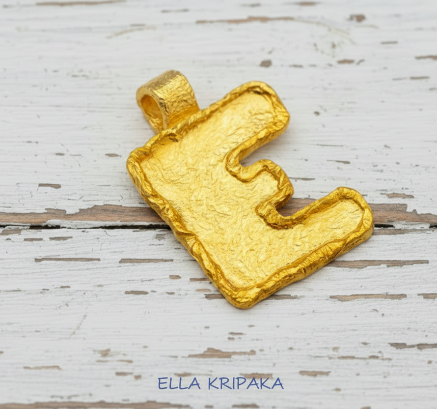 Organic 24k 9999 gold letter 'E' Initial pendant on a wooden surface with 'ELLA KRIPAKA' branding