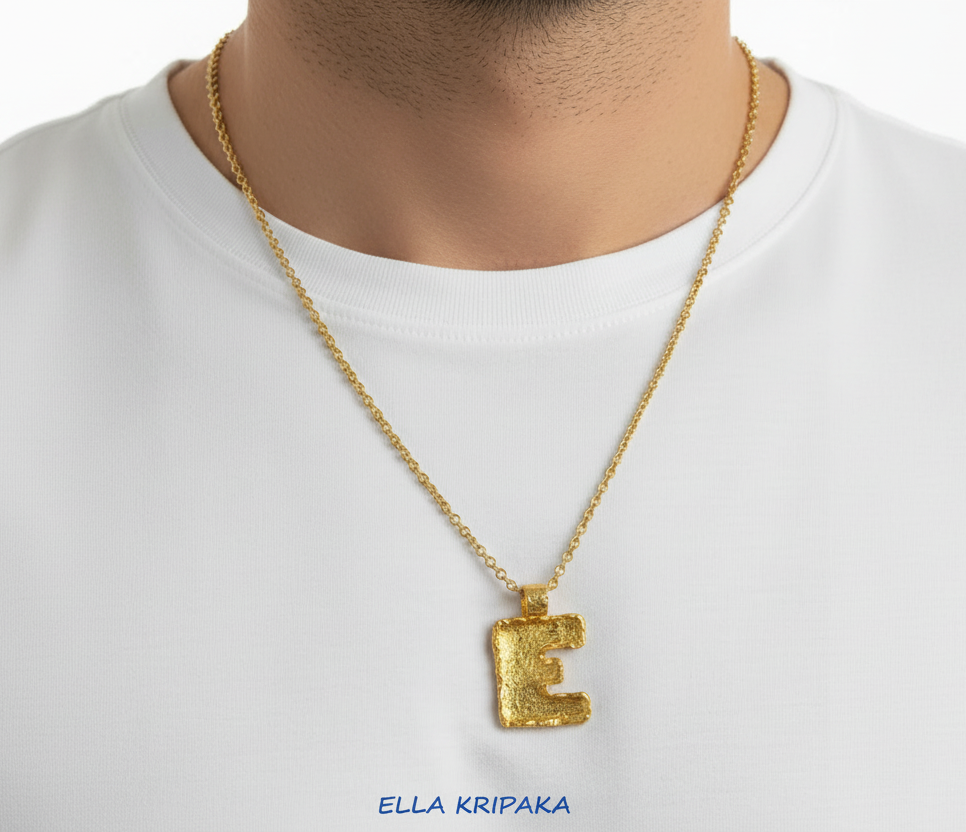 24k Gold necklace chain with organic initial letter 'E' pendant on a perdon in a white t-shirt, branded 'Ella Kripaka'.