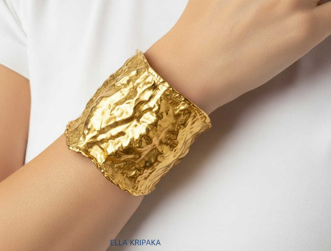 Organic 24k gold hammered wavy cuff large bracelet with thick uneven textured borders is on woman's wrist, branding artist-jeweler name 'Ella Kripaka'