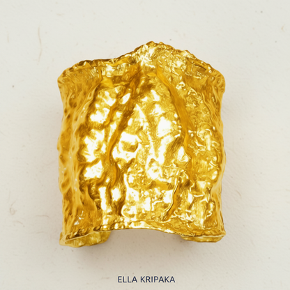 Shiny textured 24k gold cuff bracelet with a hammered, organic surface, displayed on a craft white paper background with the brand name 'ELLA KRIPAKA' printed below
