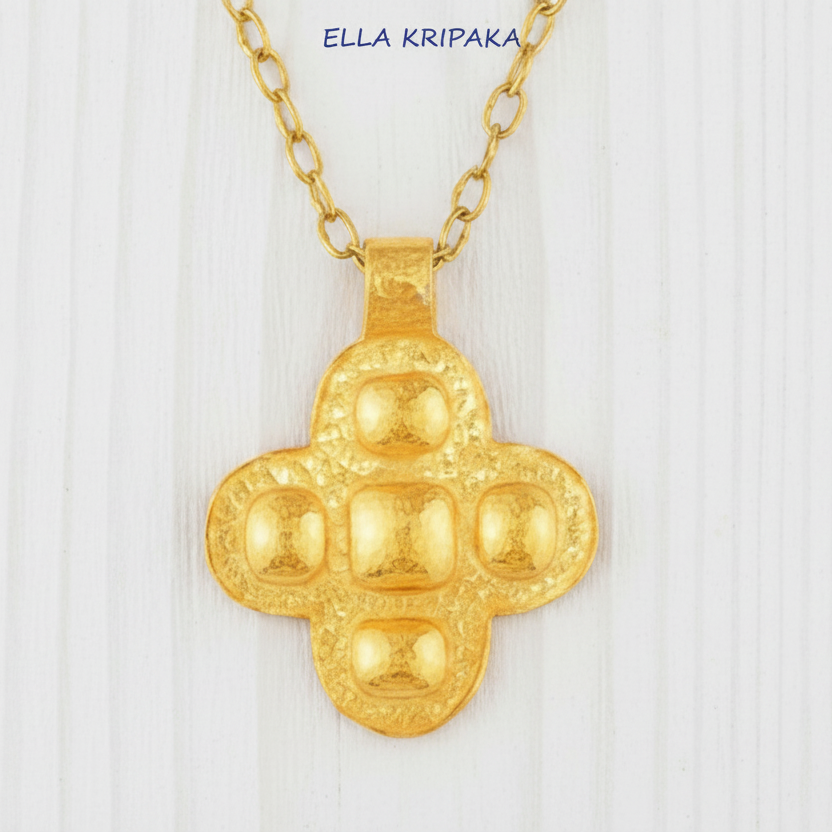 24k 9999 gold hammered Byzantine cross pendant with forged gold textures is on a white wooden surface, artist's name 'Ella Kripaka'