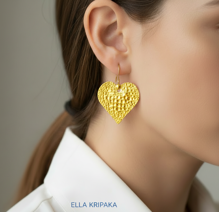 Organic 24k 9999 gold hammered heart earrings with shiny gold textures are worn by a model on neutral background, artist-jeweler's name 'Ella Kripaka'