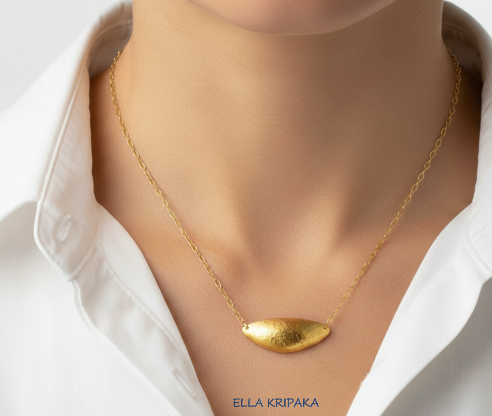 24k 9999 gold hammered dome pendant with forged gold textures and with chain is wearing on person in white shirt, artist's name 'Ella Kripaka'